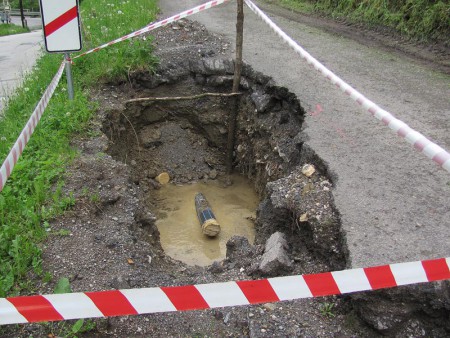 Pod kostolom vyhĺbená jama so zapichnutou rúrou a rozpadajúci sa okraj cesty k fare (máj 2015)